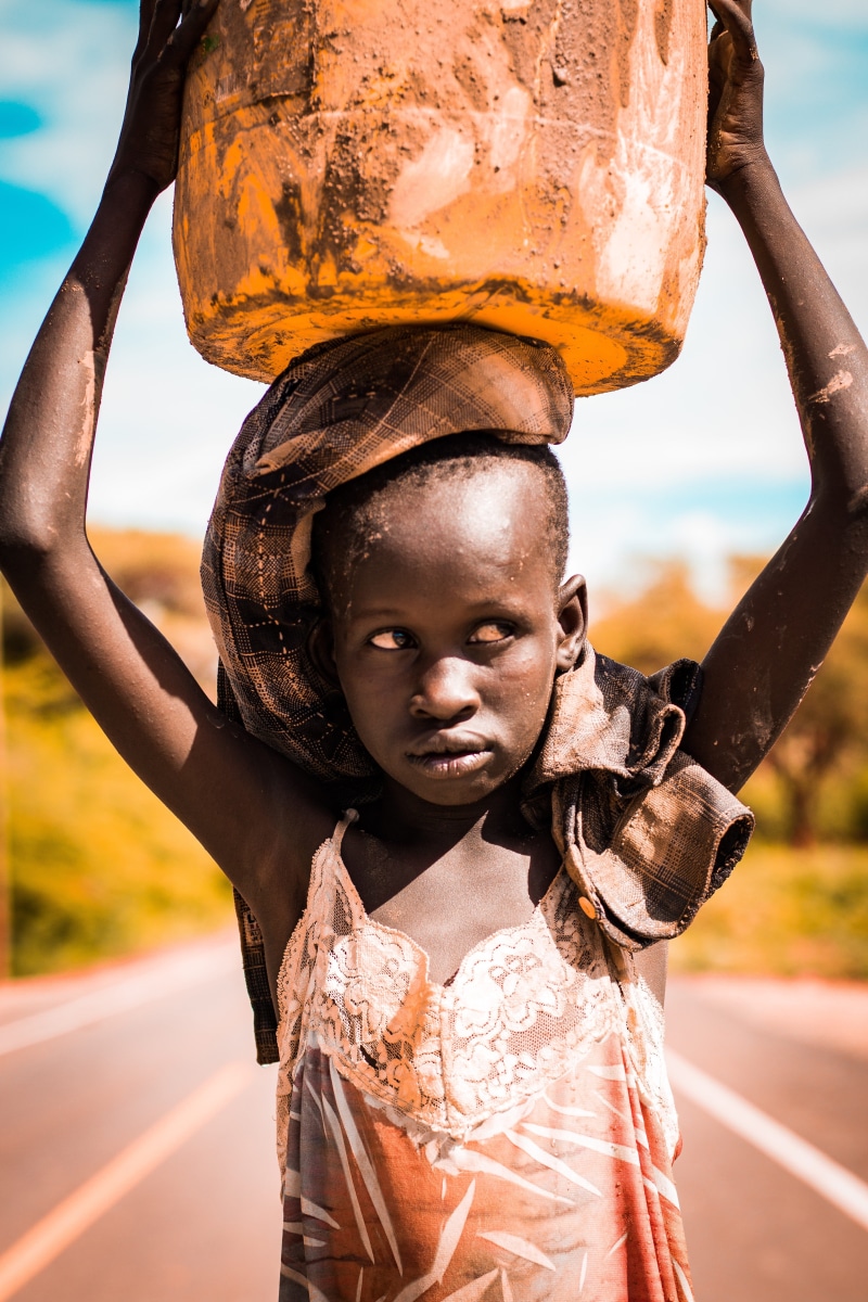 sunlight, day, transportation, jerrycan, sad, girl, cinematic, statue, focus on foreground, outdoors, real people, face, teal, african, 5K, orange, sculpture