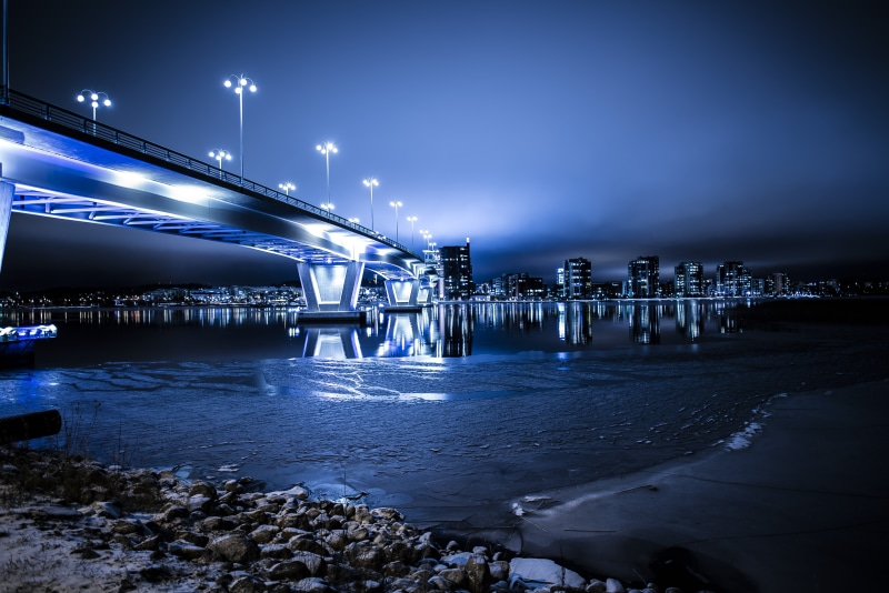 5K, blur, outdoors, reflection, rocks, blue, building exterior, transportation, city, futuristic, evening, street lights, buildings, water, shore, transportation system