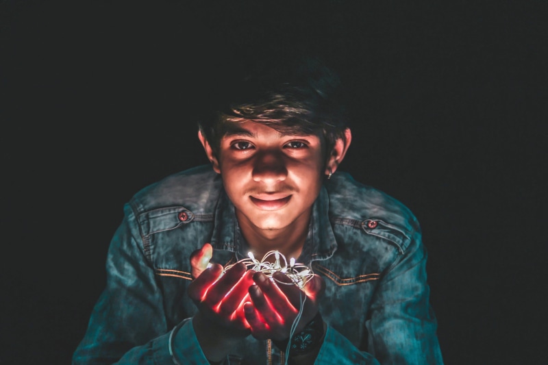indoors, wear, waist up, string lights, front view, holding, black background, man, face, white, looking at camera, smiling, one person, 5K, portrait