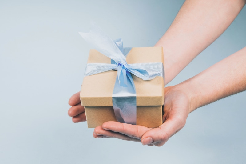 package, celebration, blue background, ribbon - sewing item, box, close-up, hand, wrapping paper, studio shot, body part, human limb, indoors, surprise