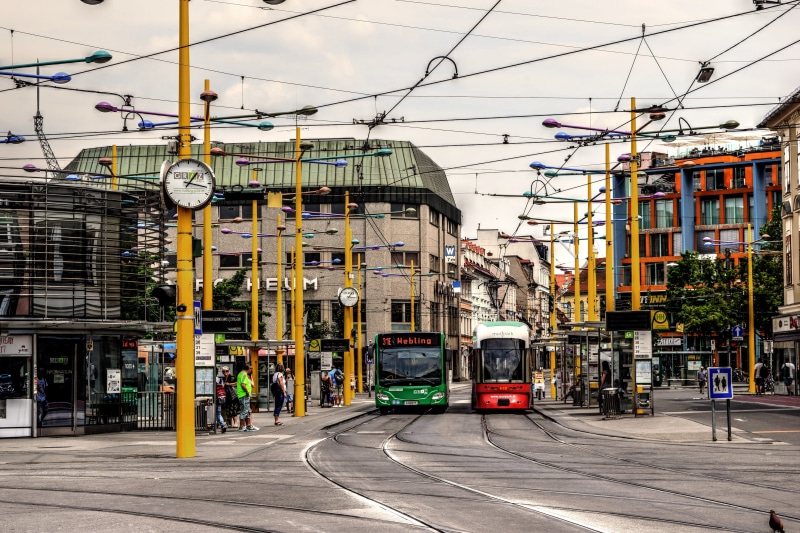 electricity, architecture, jakominiplatz, green, incidental people, building exterior, cable car, tram, two, street, public transportation, motor vehicle