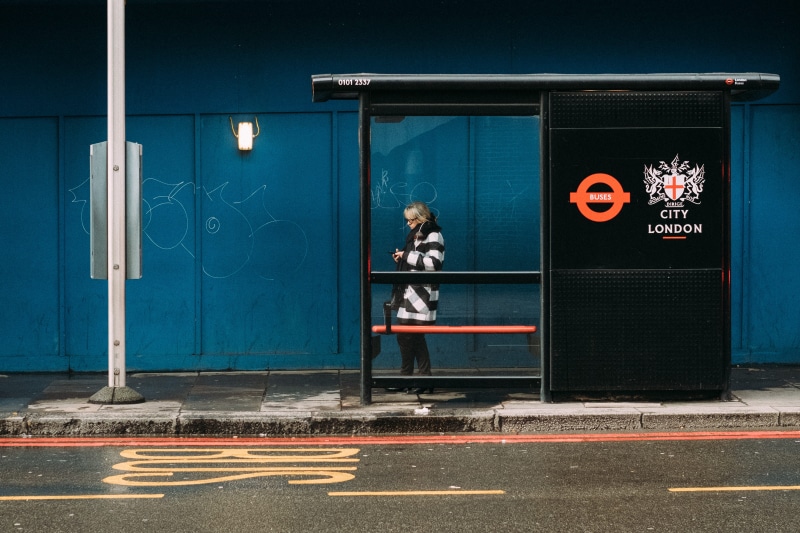 bus, sidewalk, urban, fujifilm, graffiti, entrance, women, phone, street, bus stop, business, city, waiting, public space, standing, urban Scene, person