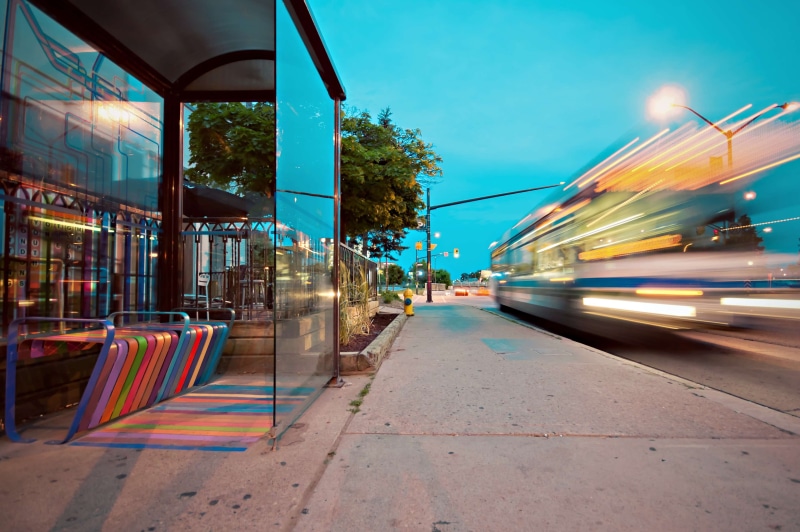 road, land vehicle, transport, motion, bus stop, blurred motion, built structure, public transportation, transportation, sidewalk, bench, rail transportation