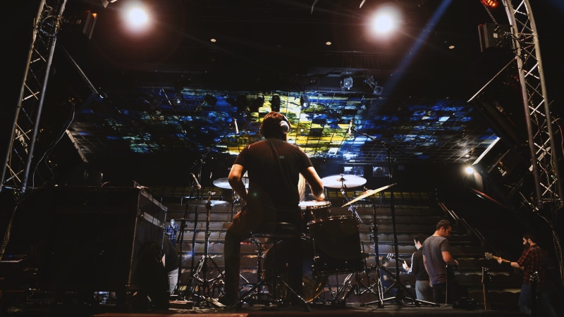 musical equipment, drums, nightlife, stage - performance space, lighting, guitar, musician, crowd, performance, entertainment occupation, drummer, rear view