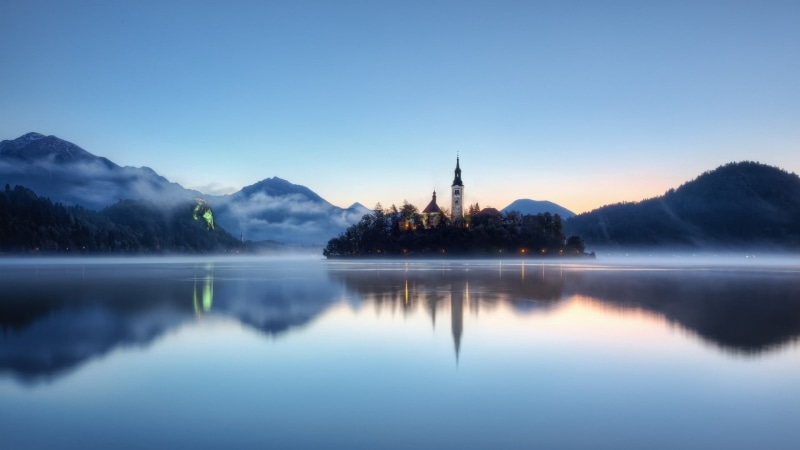 religion, belief, mountain, no people, mountains, landscape, place of worship, island, outdoors, sky, tree, mist, built structure, cyan, church, blue, lake
