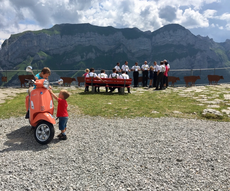 rear view, motor scooter, sky, childhood, mountain range, day, tradition, real people, men, vacations, flower, group of people, man, outdoors, eat, lifestyles