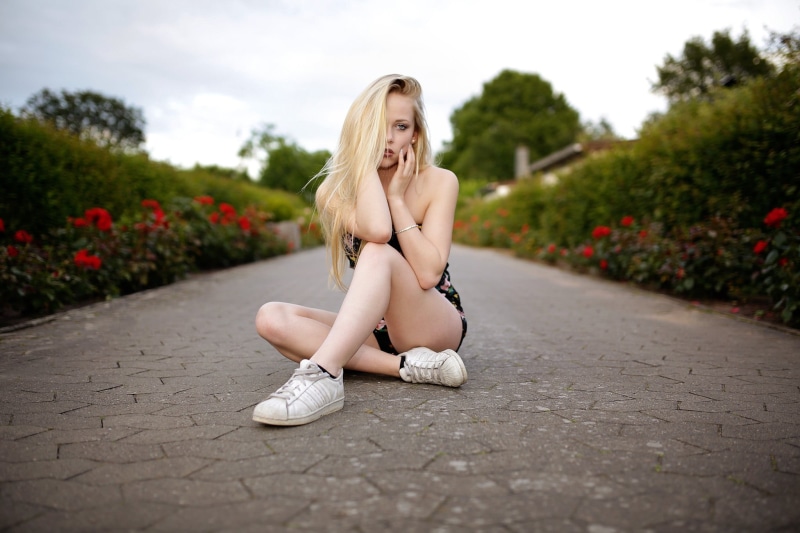 women outdoors, blond hair, depth of field, blonde, plant, lifestyles, beautiful woman, outdoors, city, sneakers, looking at camera, one person, hairstyle