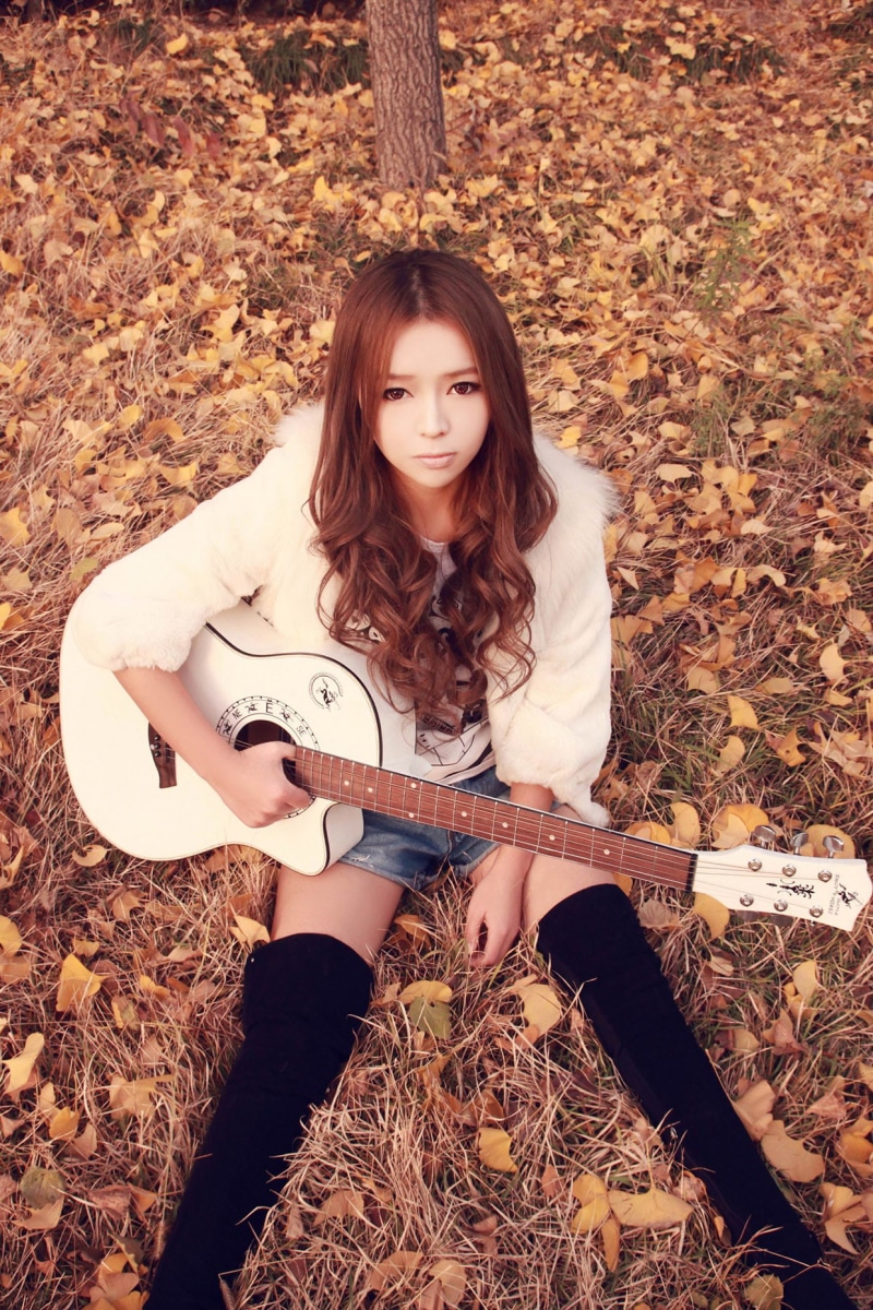 720P, real people, one person, looking at camera, model, sitting, day, jean shorts, front view, women outdoors, fallen leaves, musical instrument, young adult