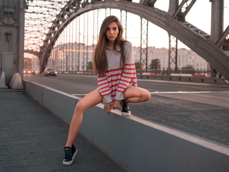 neck, front view, looking at camera, tanned, women outdoors, sweater, bridge, outdoors, bridge - man made structure, 2K, sneakers, one person, striped