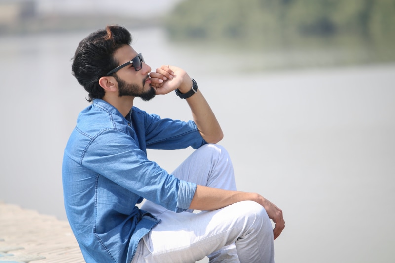 three quarter length, outdoors, day, young adult, mans fashion, sitting, model, glasses, adult, fashion, side view, hairstyle, guy, young men, male model