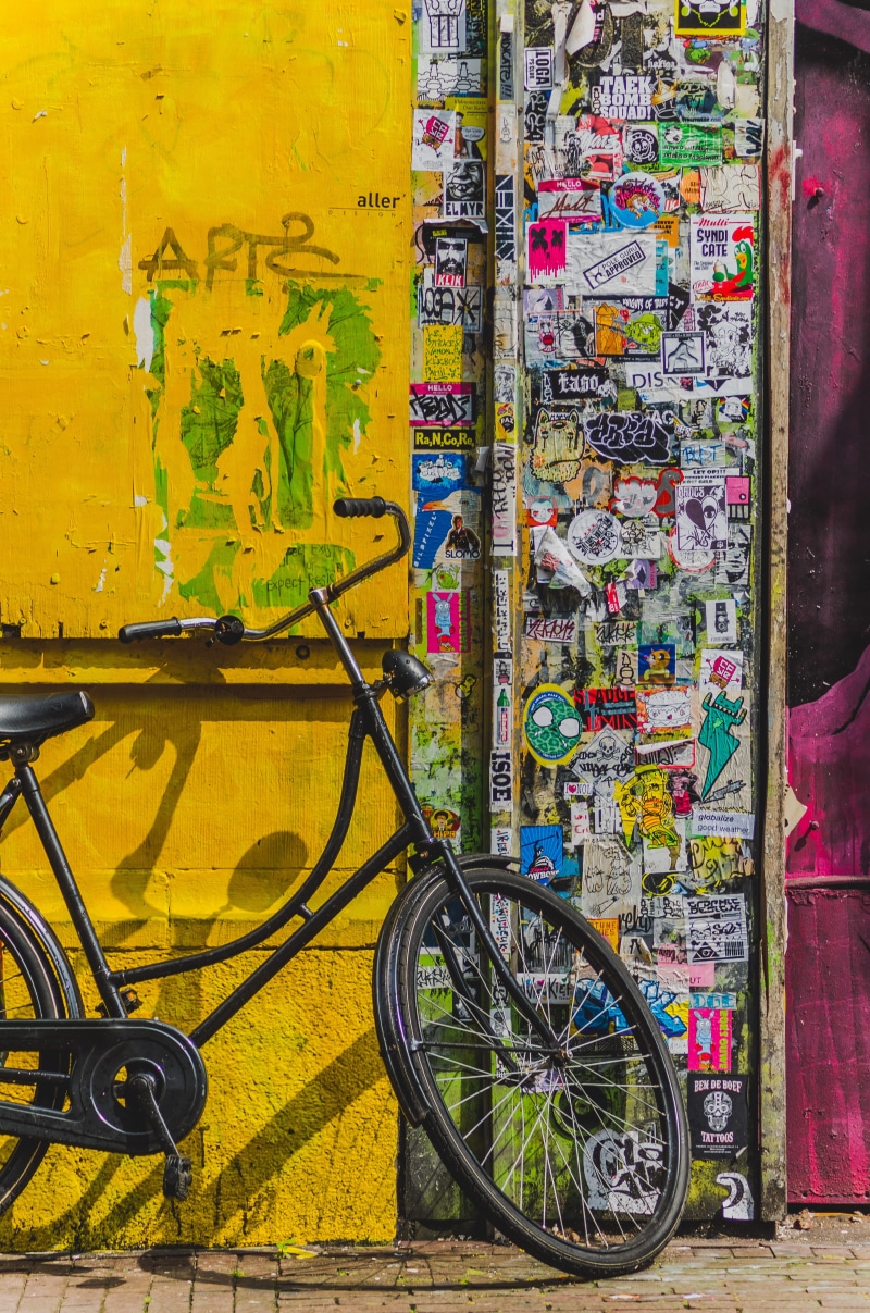 stationary, wall - building feature, 4K, street, outdoors, stickers, day, city, bicycle, multi colored, black, no people, bike, yellow, wheel, transportation