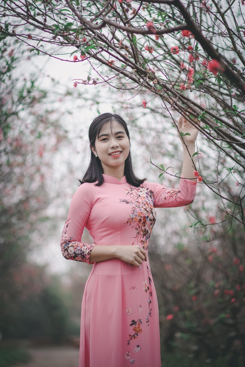 young adult, front view, flowering plant, standing, women, attractive, facial expression, one person, person, pink color, three quarter length, plant, traditional wear