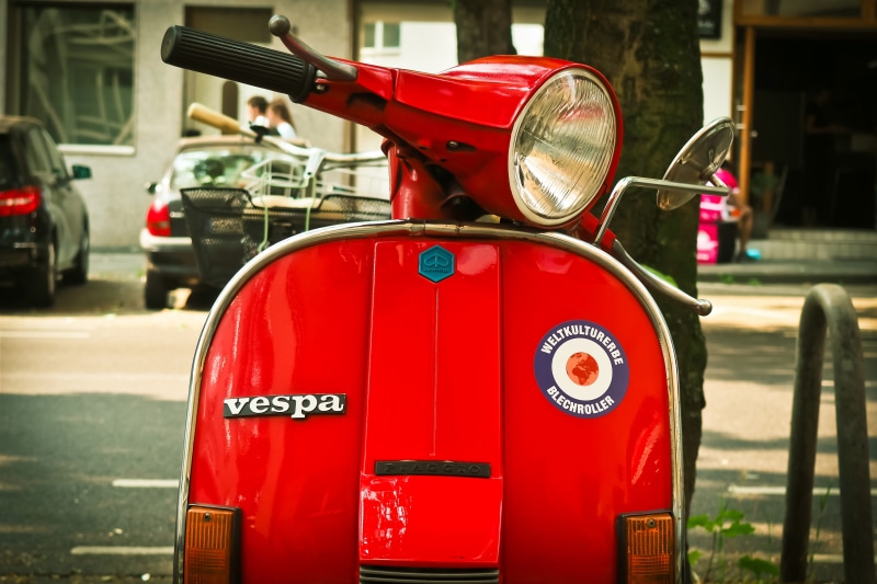 motor scooter, focus on foreground, day, mode of transportation, transportation, land vehicle, vespa, motor, text, car, vehicle, old, stylish, locomotion