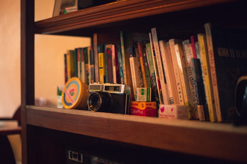 wooden shelves, book bindings, old camera, collection, home interior, antique, film, research, library, wisdom, 5K, book, school, order, bookcase, room