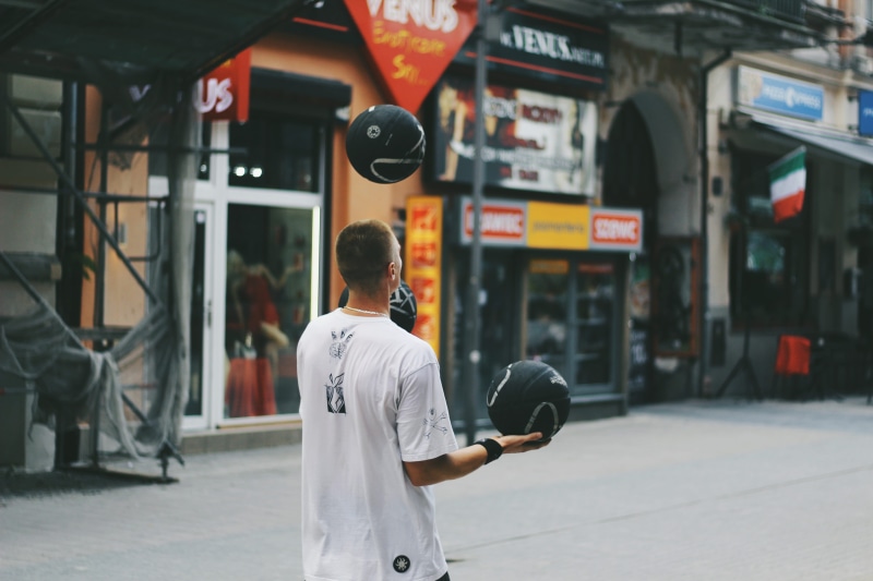 communication, standing, stores, adult, lifestyles, focus on foreground, juggling, city, person, action, juggler, buildings, one person, near, pavement