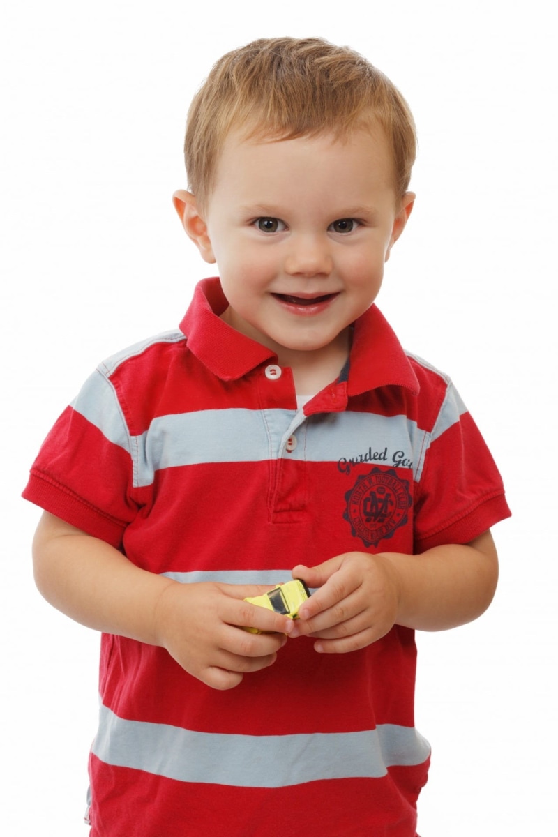 person, car, adorable, red, toy car, indoors, shirt, polo, standing, yellow, toddler, childhood, cute, kid, one person, emotion, smiling, children only
