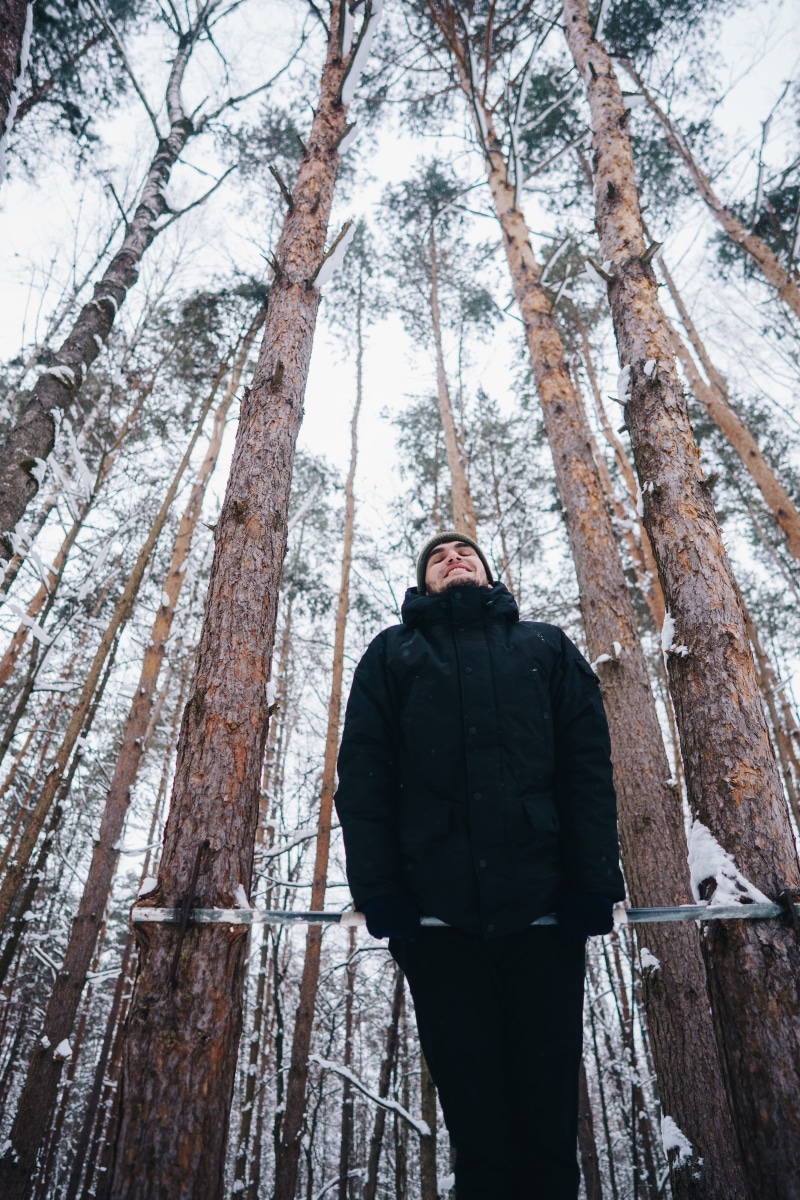 smile, snow, woodland, outdoors, tree trunk, front view, conifer, lifestyles, three quarter length, trunk, warm clothing, person, land, jacket, forest