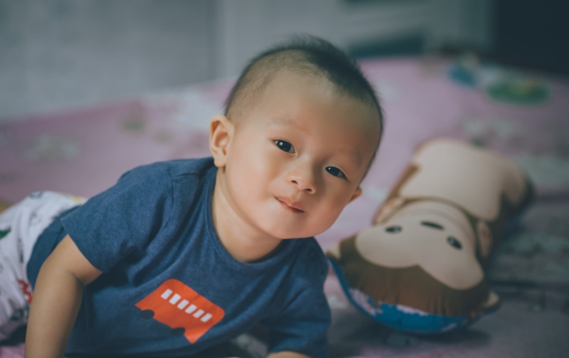 depth of field, bolster, adorable, boys, child, close-up, focus on foreground, 4K, indoors, smile, toddler, casual clothing, infancy, focus, near, lying