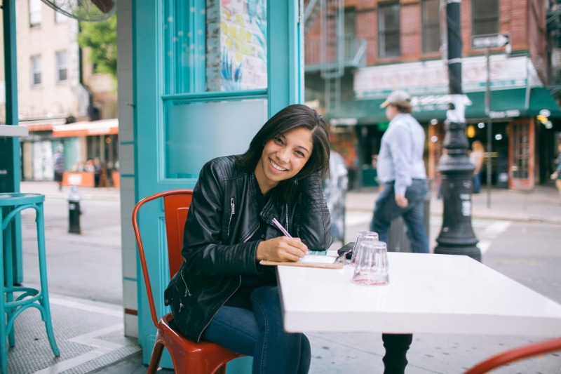 outdoors, real people, chair, focus on foreground, smile, young women, street, lifestyles, incidental people, sitting, road, sidewalk cafe, facial expression