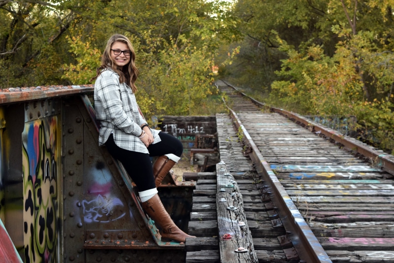 front view, dress, one woman only, train tracks, model, hairstyle, shirt, rail, leisure activity, sitting, road, adults only, portrait, female, emotion