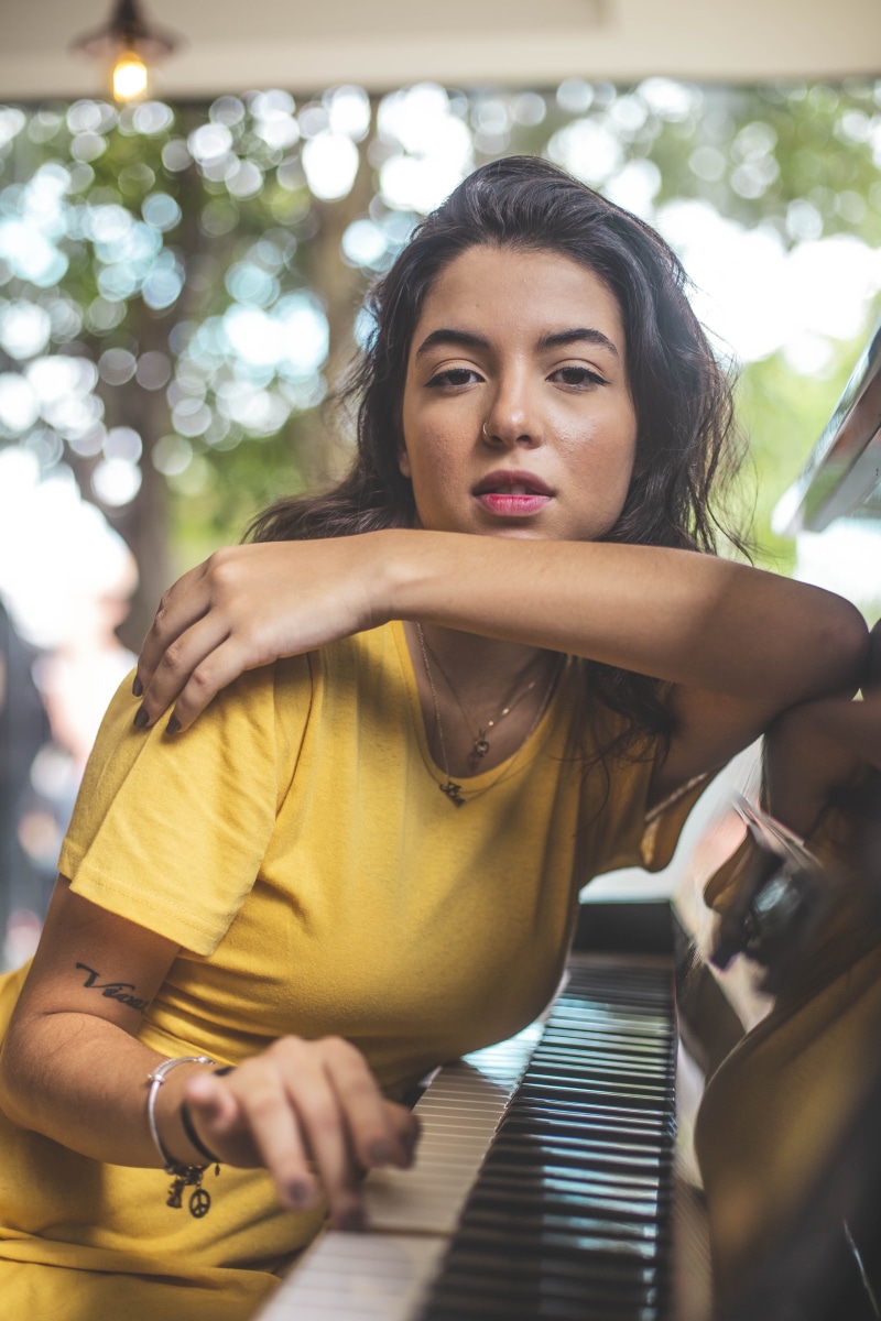 hairstyle, colors, close-up, fashionable, wear, leaning, looking, waist up, beauty, sitting, musical instrument, beautiful, daylight, looking away, hands