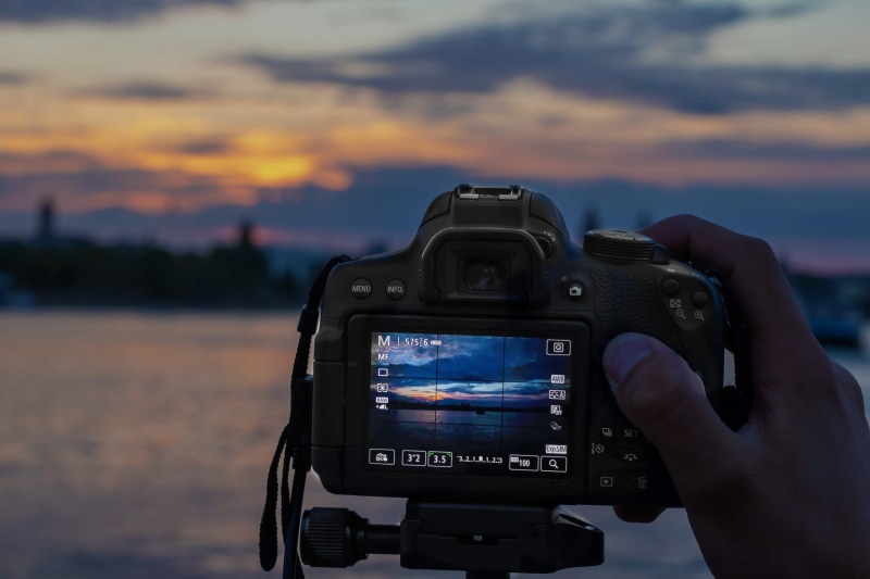 one person, sky, slr camera, human body part, digital single-lens reflex camera, holding, sunset, liveview, photographic equipment, photographing, city