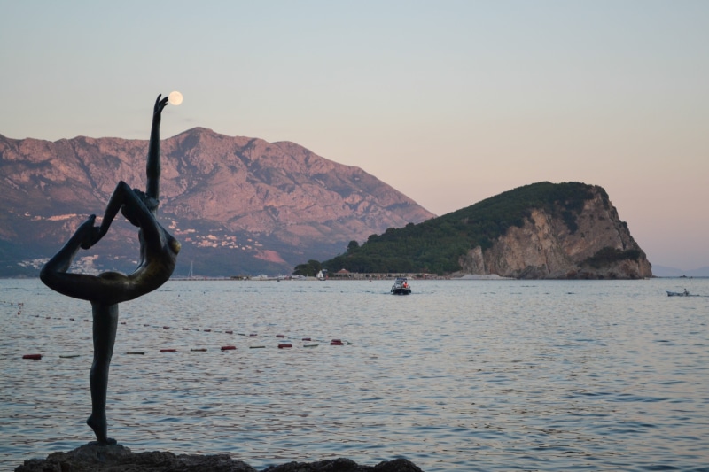 arms raised, waterfront, outdoors, beauty in nature, sky, land, budva, monument, leisure activity, tranquility, clear sky, rock - object, mountain, lifestyles