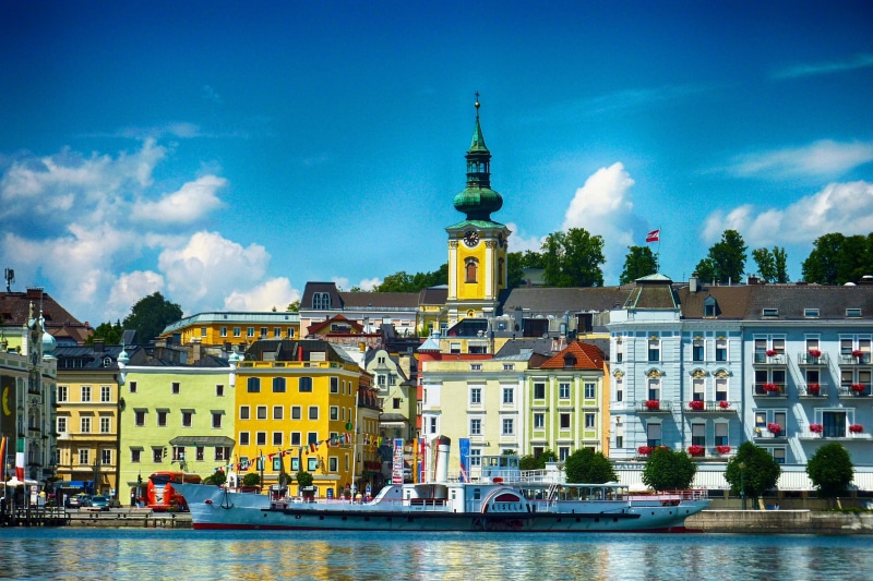 outdoors, building, passenger craft, river, sky, building exterior, 2K, tower, travel destinations, austria, place of worship, city, outside, water, clouds