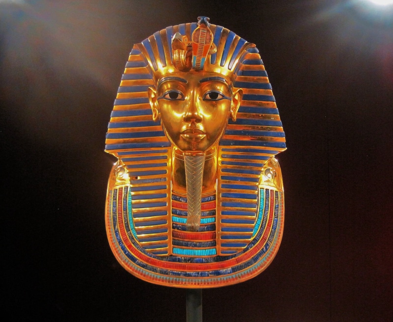 craft, male likeness, replica of king tutankhamuns mask, illuminated, gold, riches, treasure, no people, human representation, black background, ornate