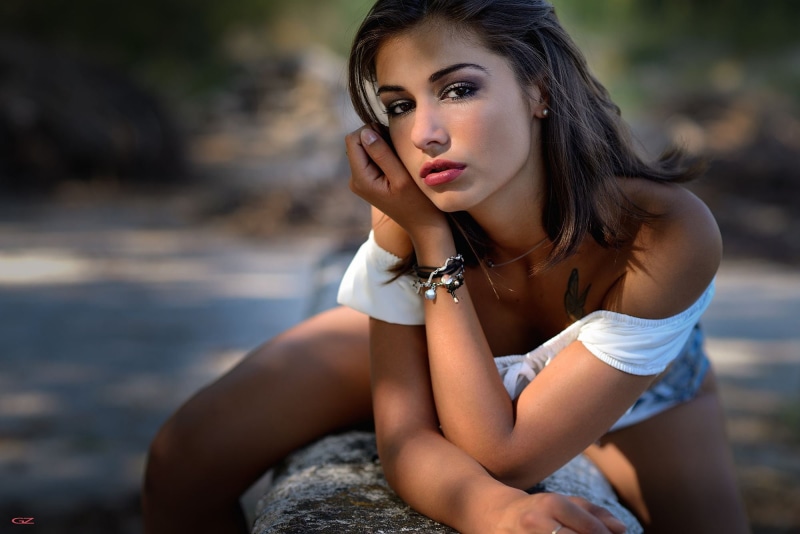 depth of field, nature, tattoo, looking at viewer, bracelets, earring, brunette, 1080P, denim, women, Giovanni Zacche, hand on face, bare shoulders, white clothing