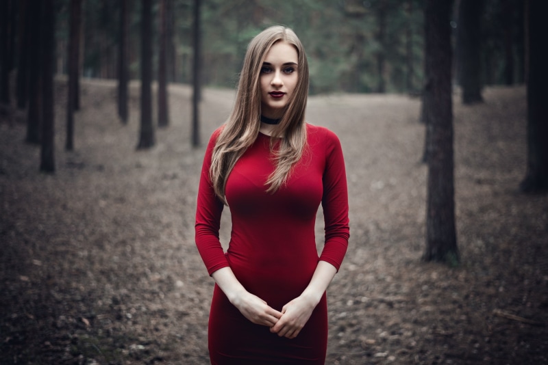 women outdoors, 2K, looking at viewer, blonde, depth of field, necklace, red dress, forest, dress, trees, model, outdoors, women, portrait