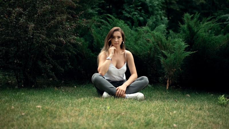 brunette, white tank top, tank top, women, portrait, cleavage, grass, bare shoulders, Vladimir Tomarov, white tops, 2K, looking at viewer, sneakers, sitting