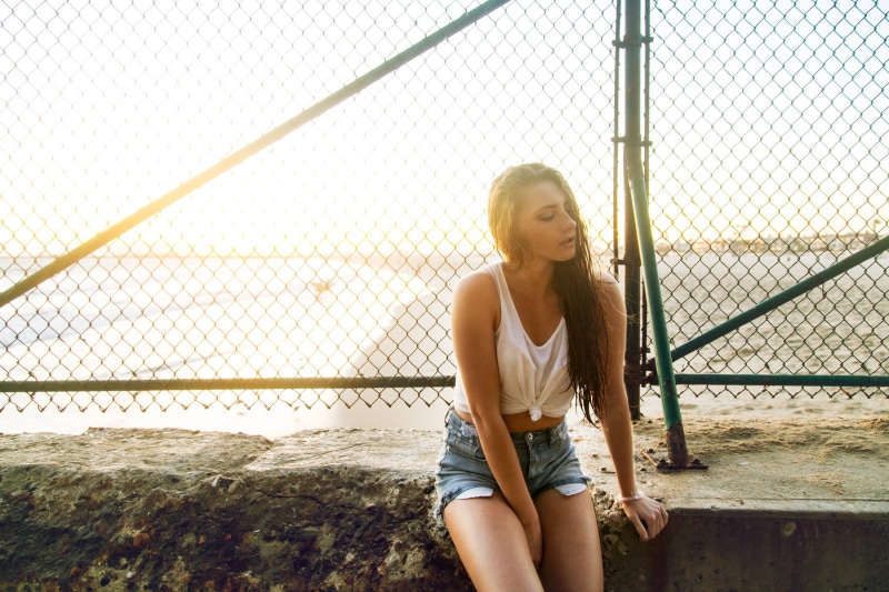 hair, long hair, sky, young adult, contemplation, day, fence, barrier, sitting, real people, tank top, sunset, beautiful woman, blonde, women, boundary