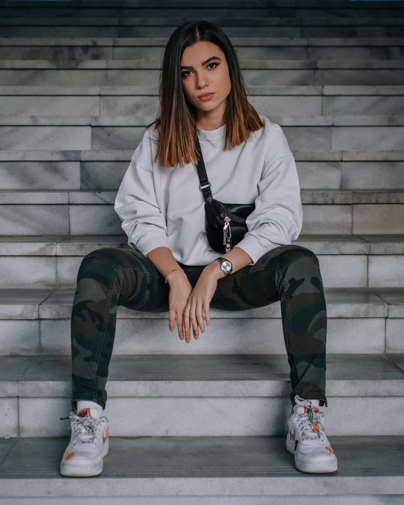 sleeve, footwear, beauty, young women, running shoe, sitting, sock, casual clothing, wall - building feature, wearing, apparel, front view, riding boot