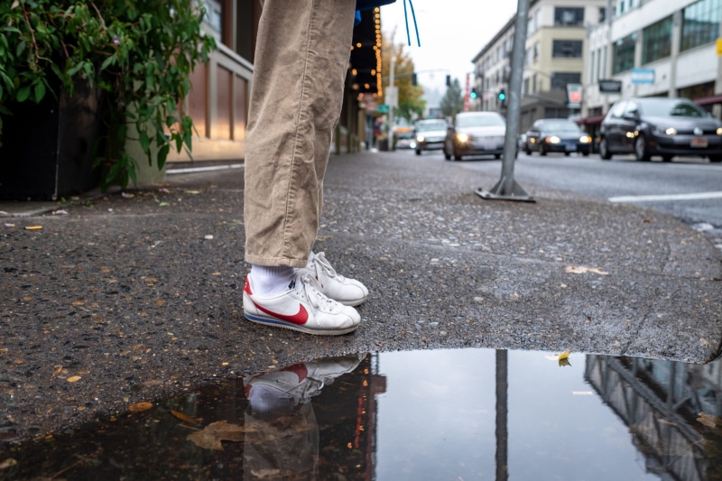 wearing, architecture, nike, pavement, mode of transportation, photo, sneakers, building exterior, person, white shoes, city, human leg, footpath, red