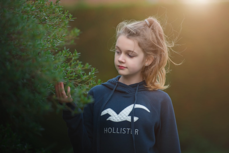 blossoms, casual clothing, happy, contemplation, child, waist up, focus on foreground, little girl, 5K, childhood, outdoors, standing, nature, text, hairstyle