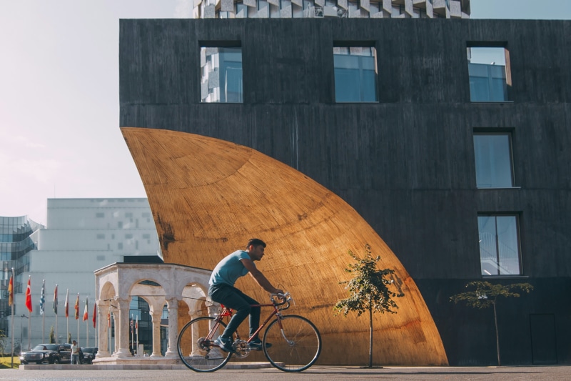 outdoors, bicycle, city, office building exterior, street, city life, men, built structure, cycling, day, sport, albania, riding, architecture, tirana