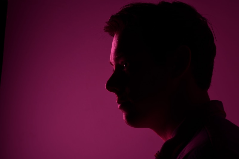 human body part, human face, contemplation, headshot, clothing, colored background, side view, nose, studio, profile view, purple, one person, apparel