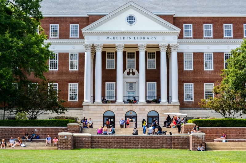 library, architectural column, crowd, seat, college, campus, adult, front, architecture, group of people, old building, men, people, built structure, text