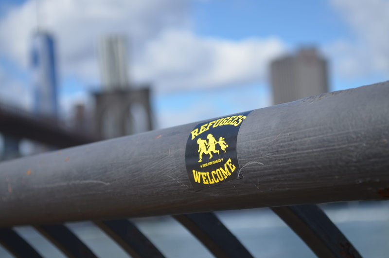 text, no people, safety, building exterior, metal, day, welcome refugees, sticker, new york, railing, 4K, outdoors, western script, nyc, architecture