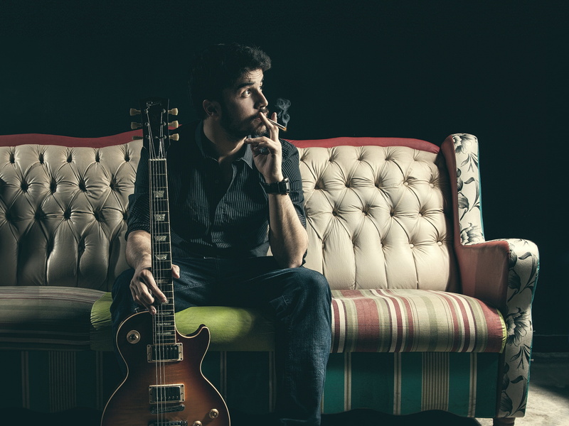 three quarter length, guitar, looking, couch, smoking, sofa, real people, young adult, furniture, leisure activity, seat, cigarettes, leather, indoors