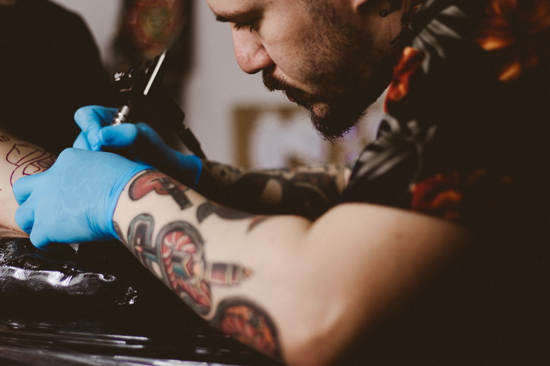 indoors, tattoo machine, tattooing, black tattoo, person, young men, tattooist, arm, young adult, focus on foreground, concentration, people, facial hair