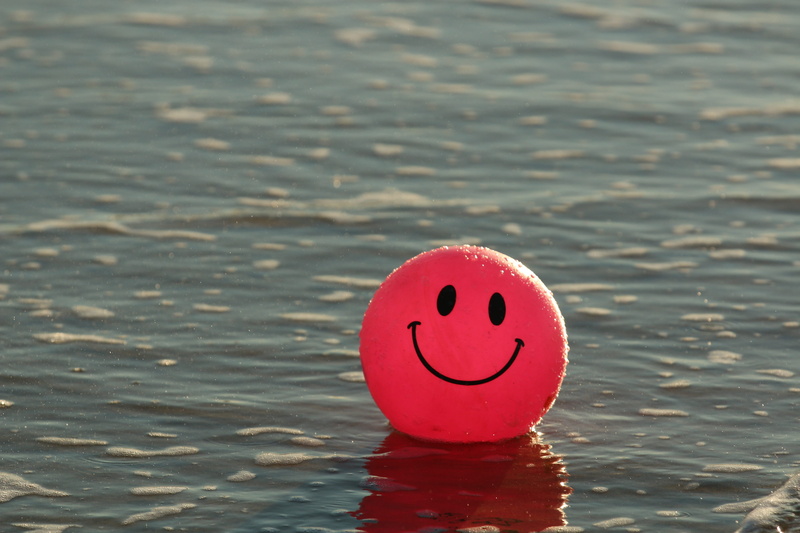no people, close-up, focus on foreground, anthropomorphic smiley face, day, face, smiley, pink, smile, ocean, inflatable, rippled, anthropomorphic, daytime