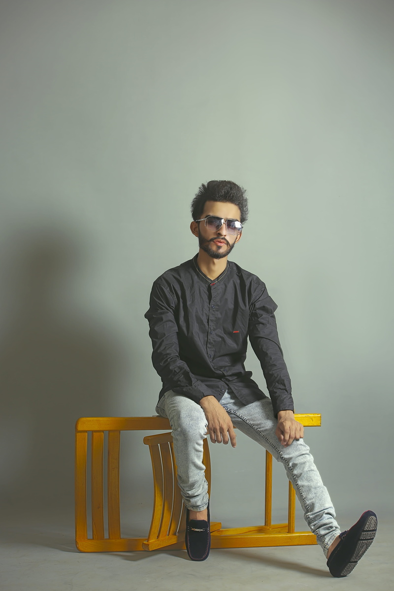 wall - building feature, fashion, looking at camera, indoors, 5K, lifestyles, seat, photoshoot, full length, casual clothing, portrait, sitting, chair
