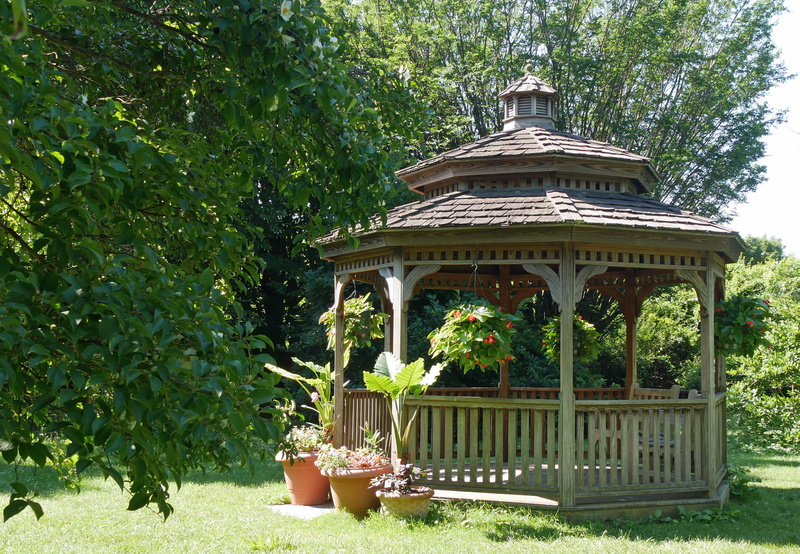 beauty in nature, architectural column, plant, sunlight, wooden gazebo, flowerbed, ornamental garden, outdoors, garden gazebo, day, small gazebo, hardtop gazebo