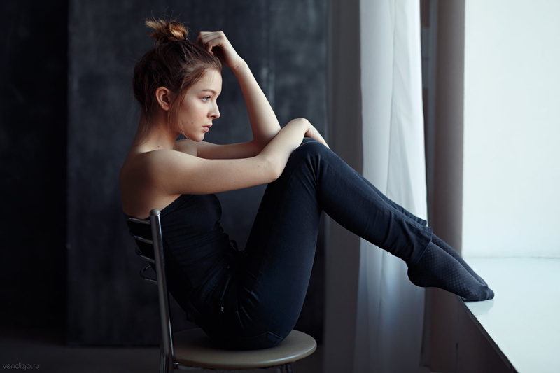 indoors, bare shoulders, chair, jeans, side view, sitting, looking away, hairbun, socks, women indoors, women, brunette, black clothing, black tops, tiptoe