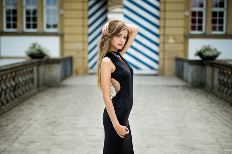 building exterior, 1080P, looking at viewer, lifestyles, blond hair, real people, side view, hands in hair, Lukas Welling, black dress, young women, outdoors