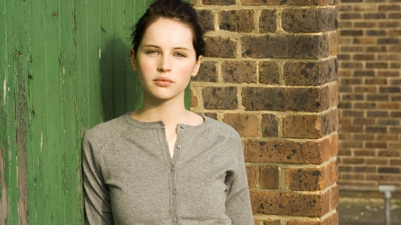 front view, young adult, brick wall, Felicity Jones, actress, looking at camera, wall - building feature, standing, lifestyles, teenager, green eyes, day