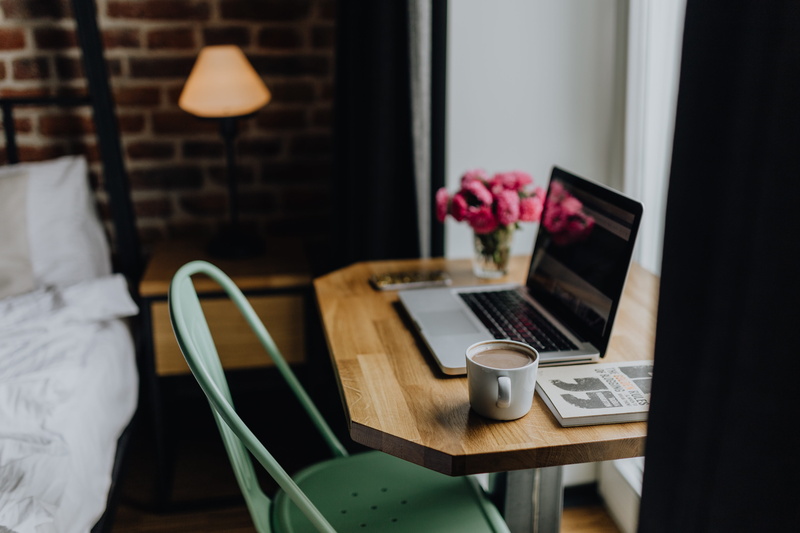 desk, computer, table, wireless technology, wooden desk, coffee, workplace, flowering plant, mug, work, food and drink, seat, laptop, electric lamp, cappucino