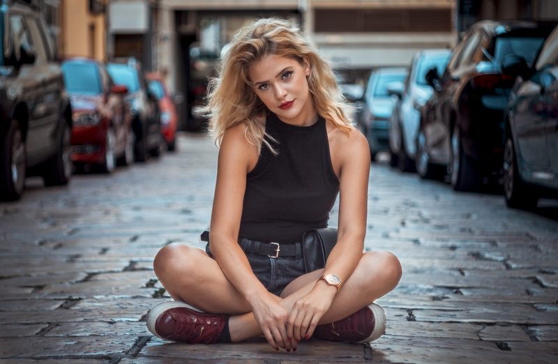 women, brown eyes, cobblestone, legs crossed, 1080P, depth of field, jean shorts, sneakers, model, hot pants, portrait, black tops, blonde, looking at